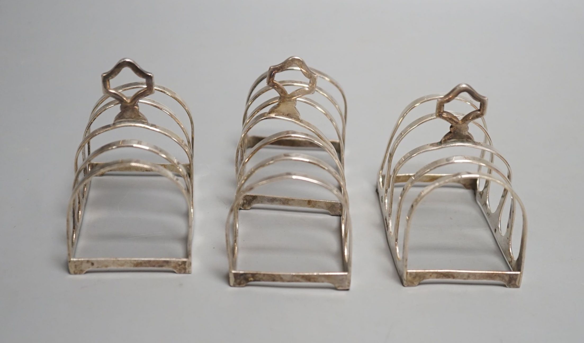 A matched suite of three silver toastracks, pair by Adie Bros. Birmingham, 1934 and larger by Goldsmiths & Silversmiths, London, 1934, 11.2cm, 162 grams.